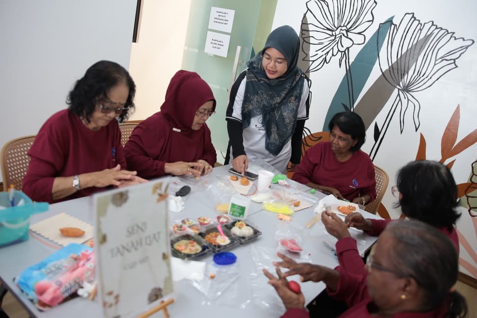 A Ruang Karya facilitator standing over a table of seated participants, guiding them through a hands-on clay session